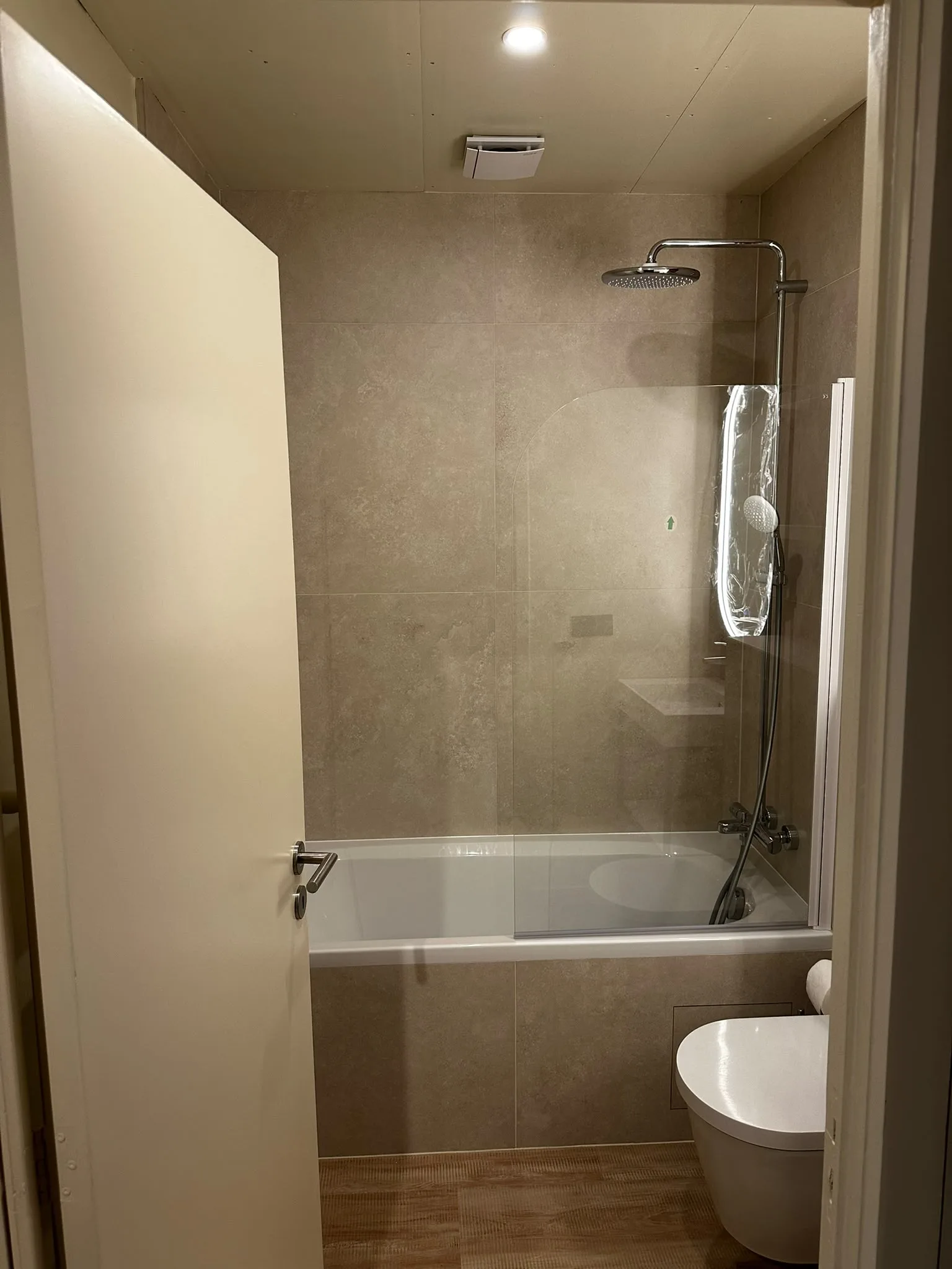 Bath with a glass screen and beige tiling