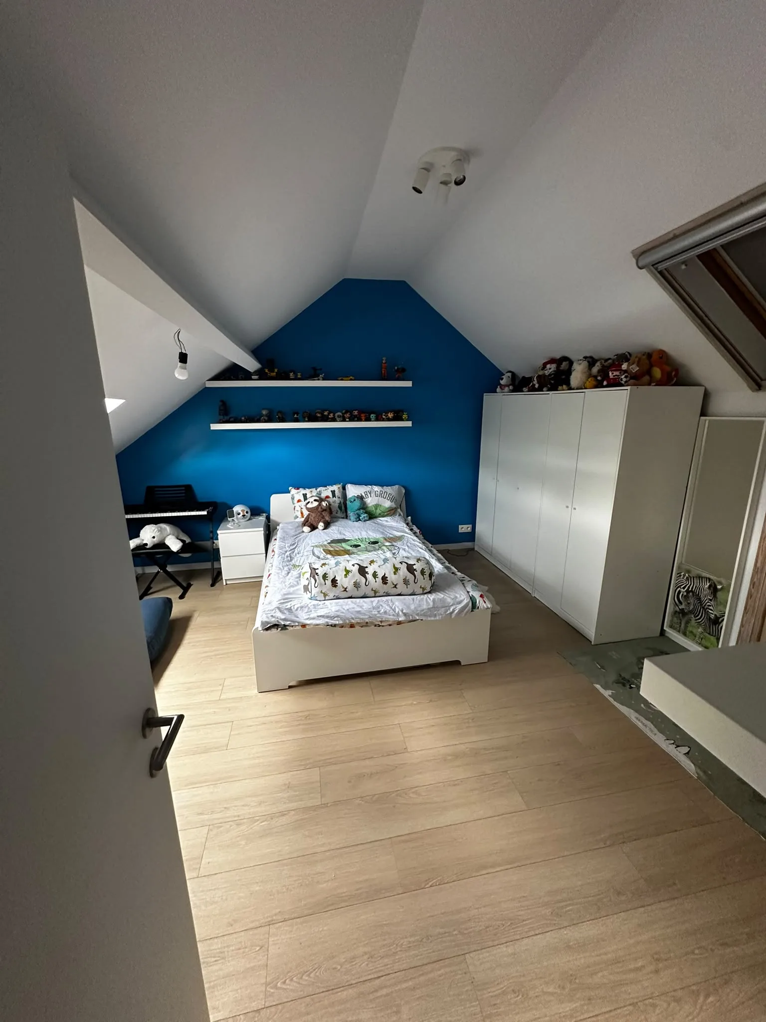 Chambre sous toiture avec mur bleu et sol aspect bois